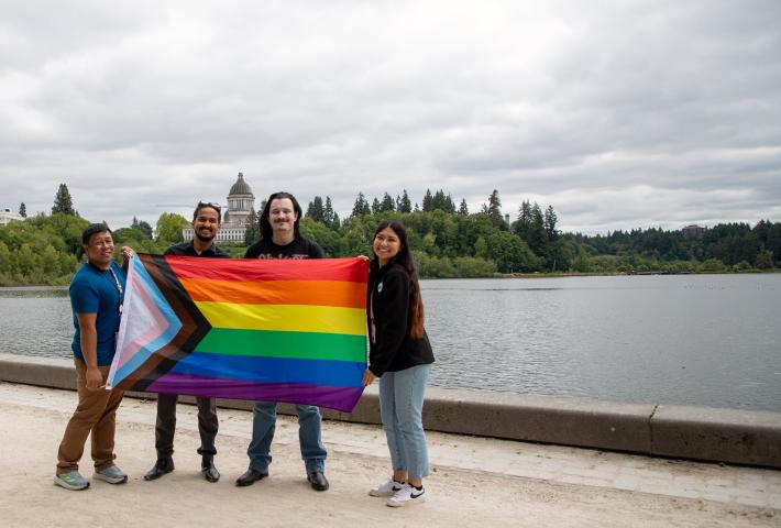 OIC staff holding up Pride flag with Capitol building in background